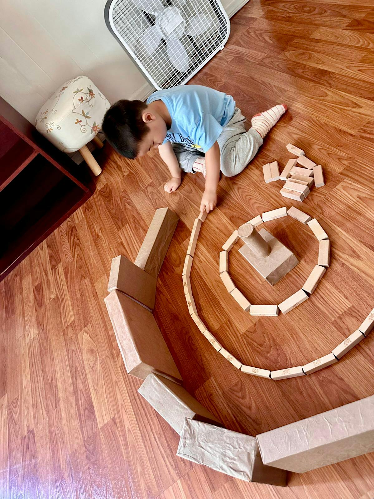 Child sitting on a wooden floor building a circular structure with blocks