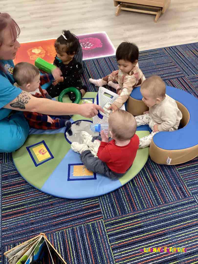 Adult and multiple young children playing with toys on a mat in a classroom