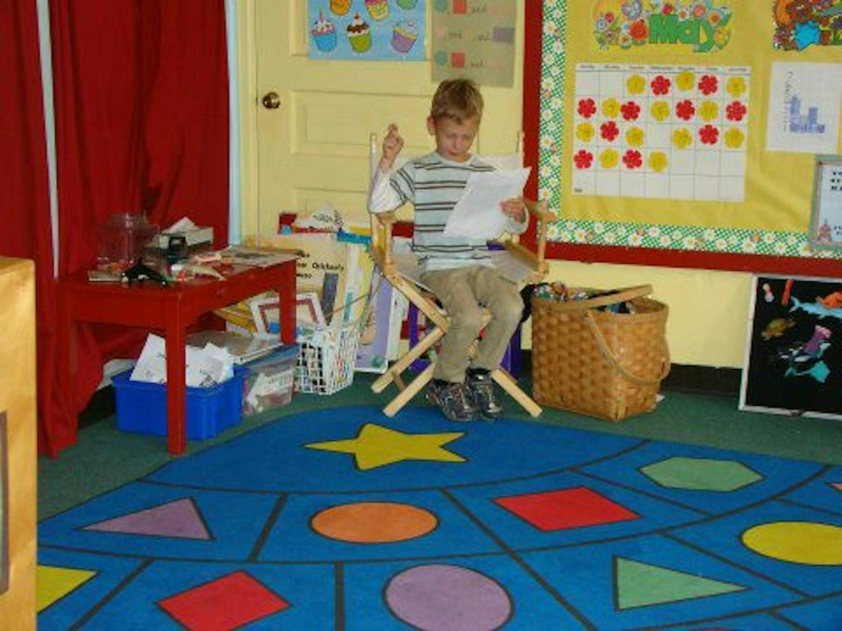 Child sitting in a chair reading a paper in a classroom