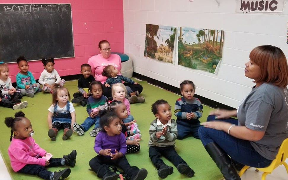 Adult speaking to a group of children sitting on the floor in a classroom