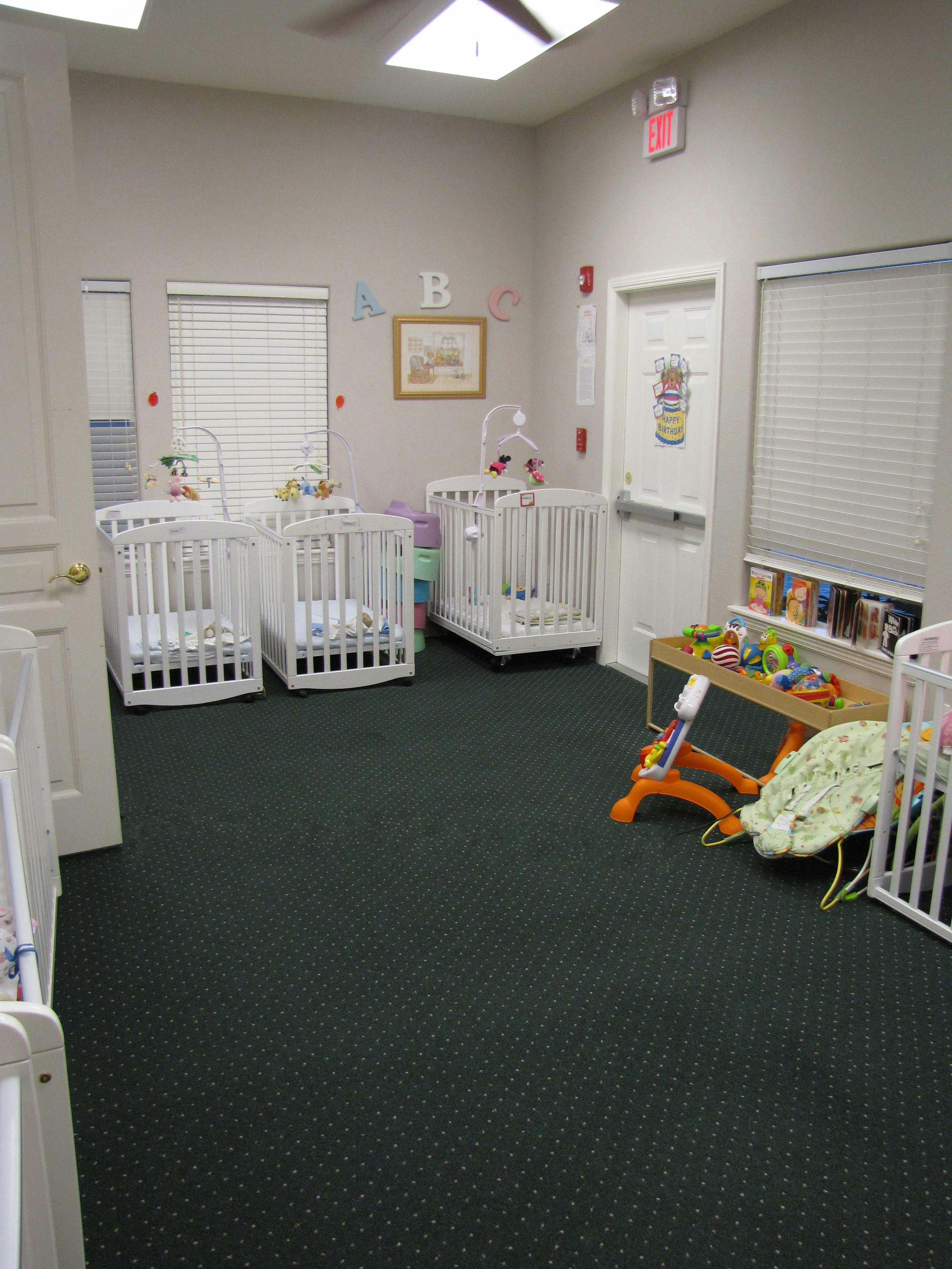 Multiple white cribs in a room with dark carpet and windows