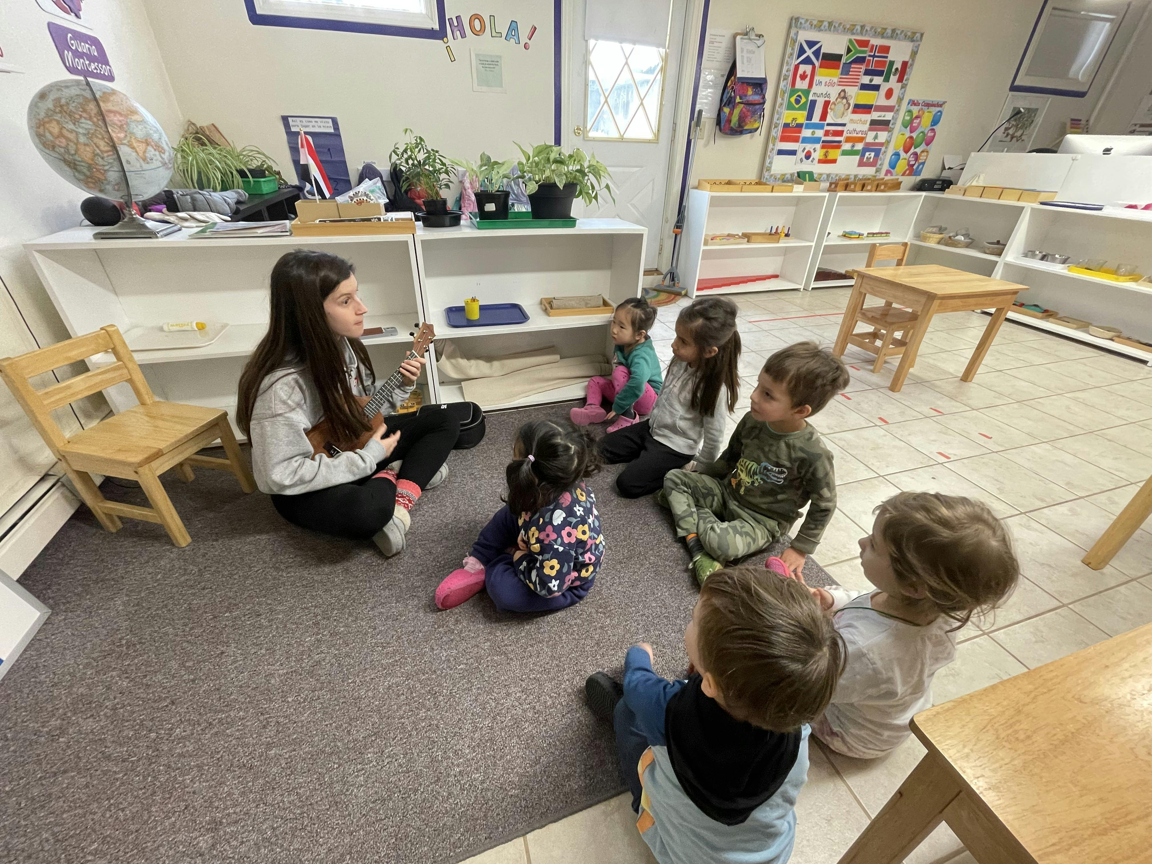 Person playing a ukulele for a group of children sitting in a classroom