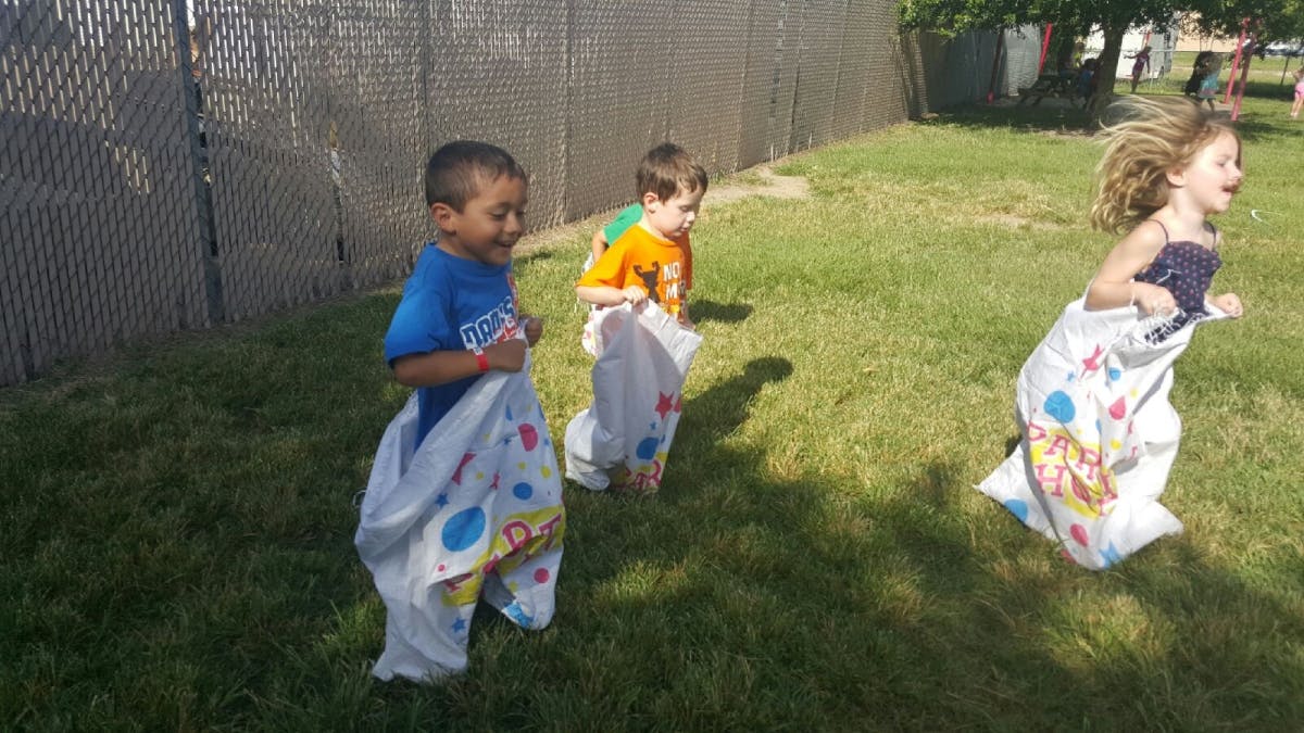 Three children in sacks participating in a sack race outdoors