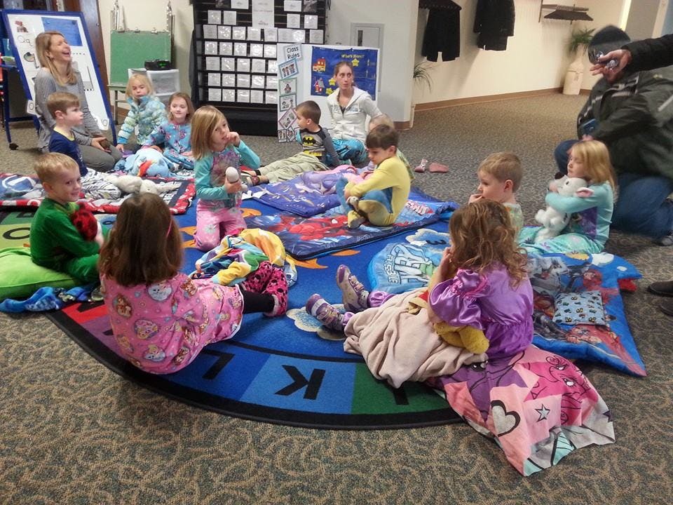 Children and adults sitting on blankets on a rug