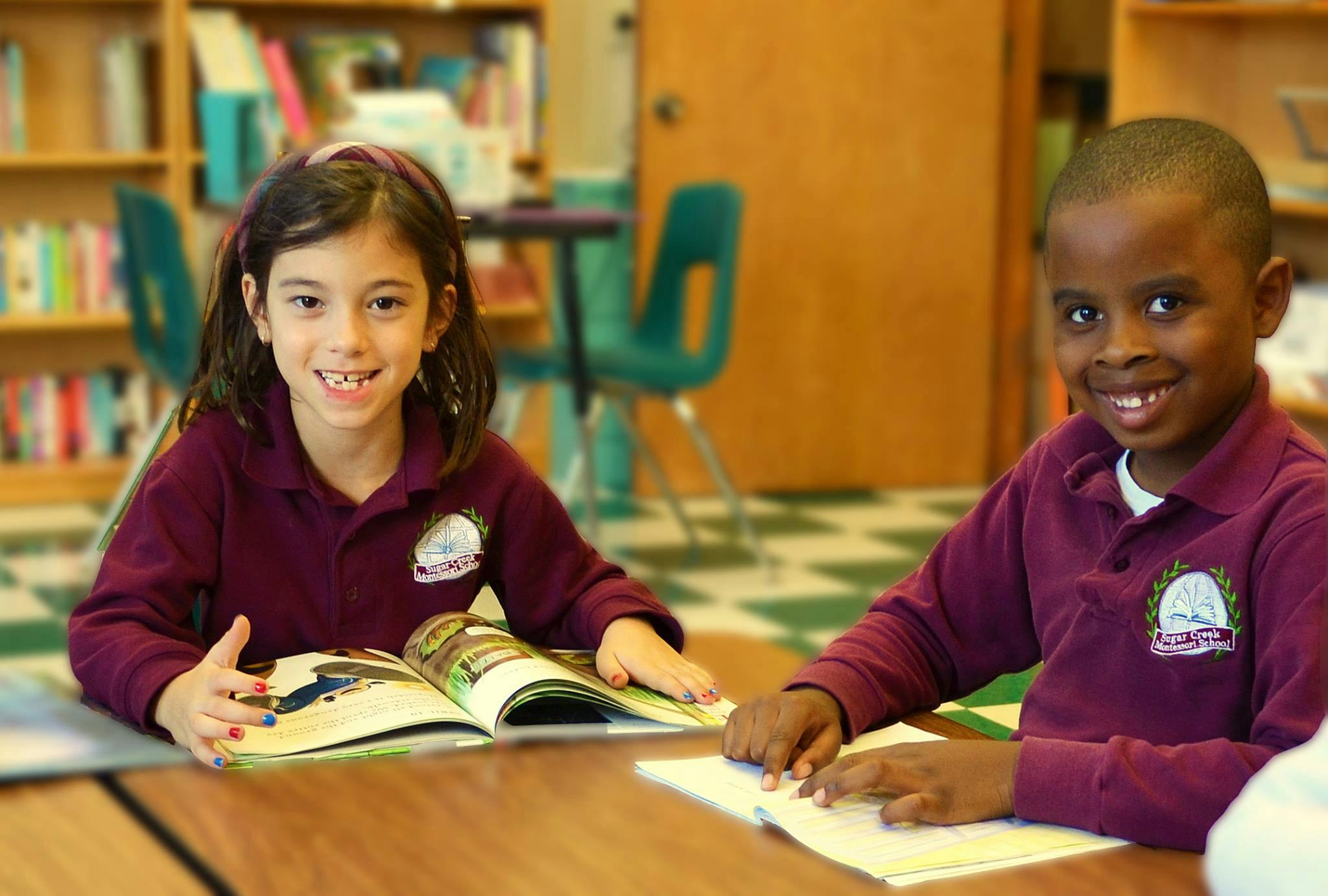Two children sitting at a table with open books in a classroom