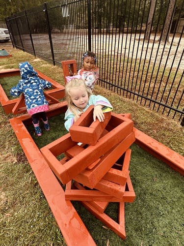 Three children playing with wooden blocks outdoors