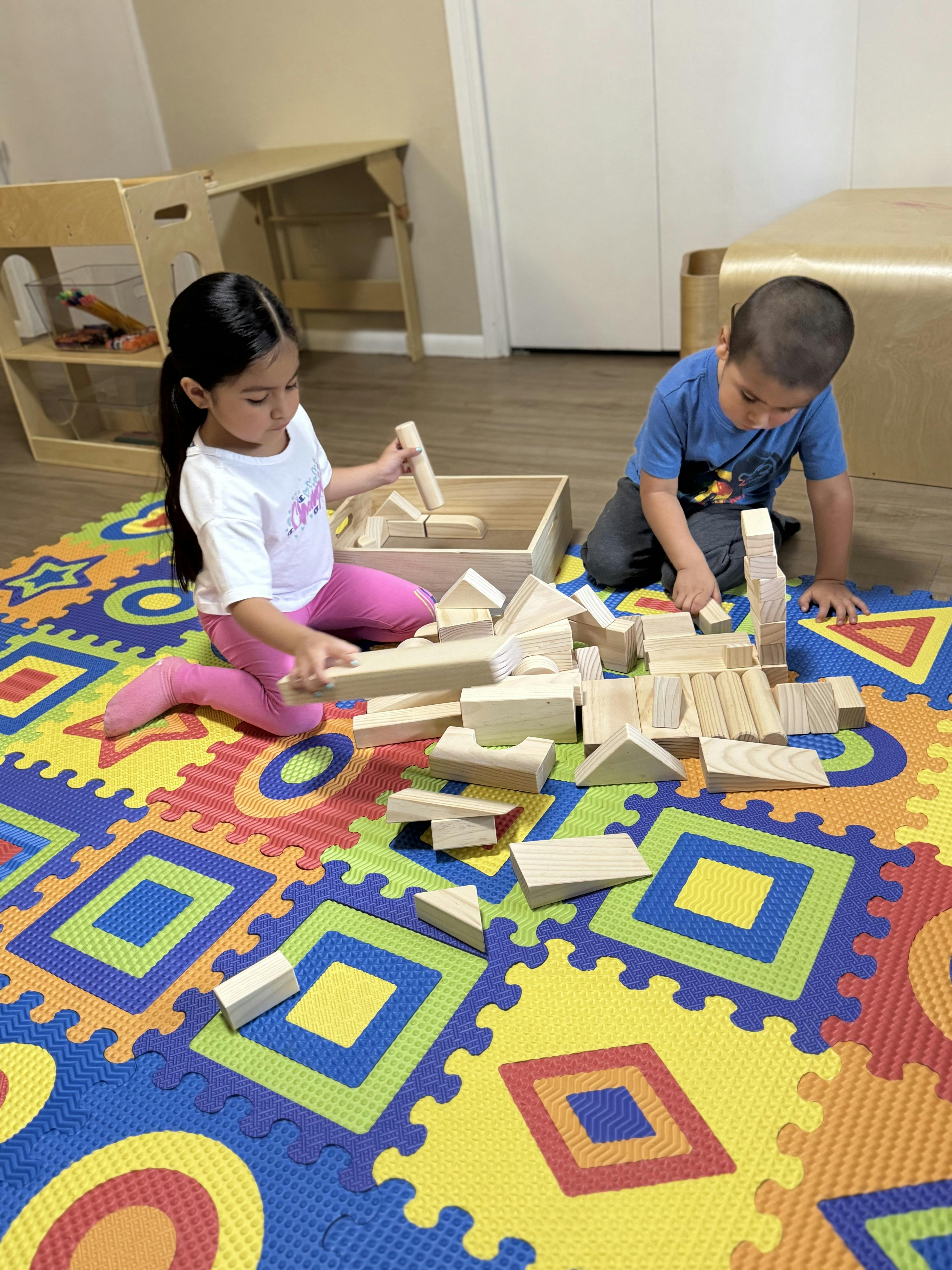 Two children playing with wooden blocks on a colorful mat