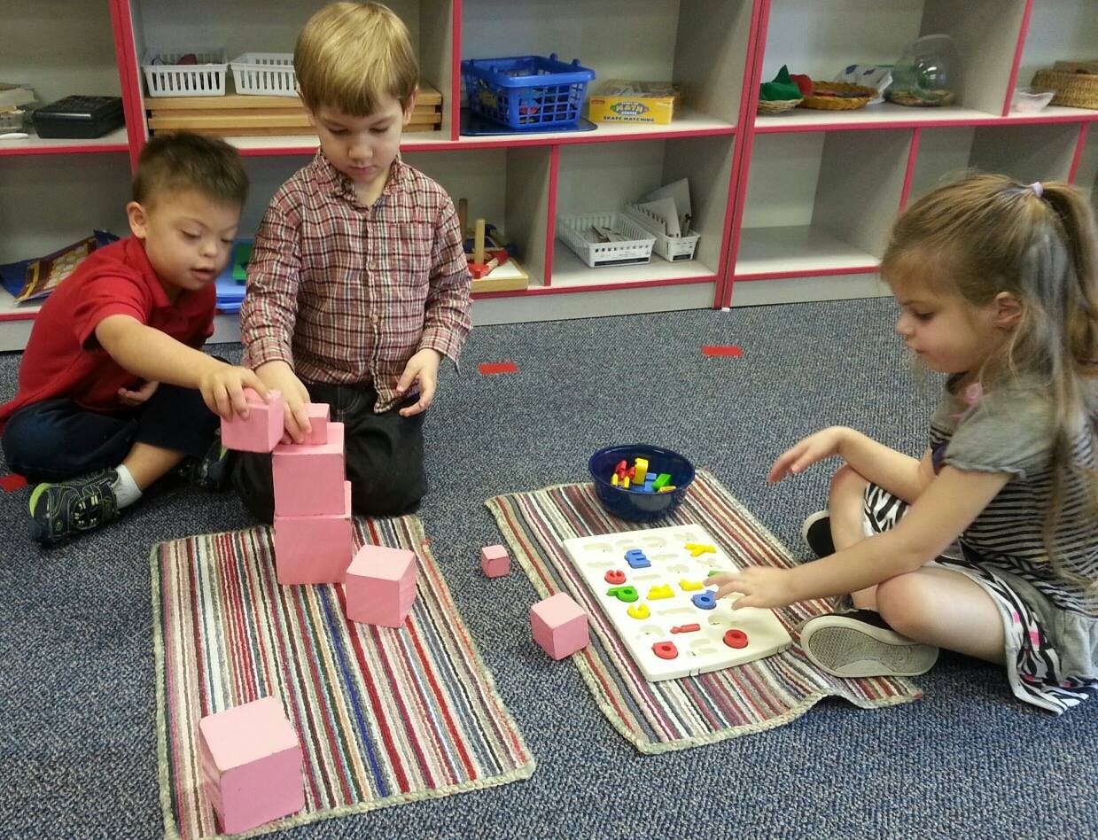 Three children playing with blocks and a puzzle on the floor