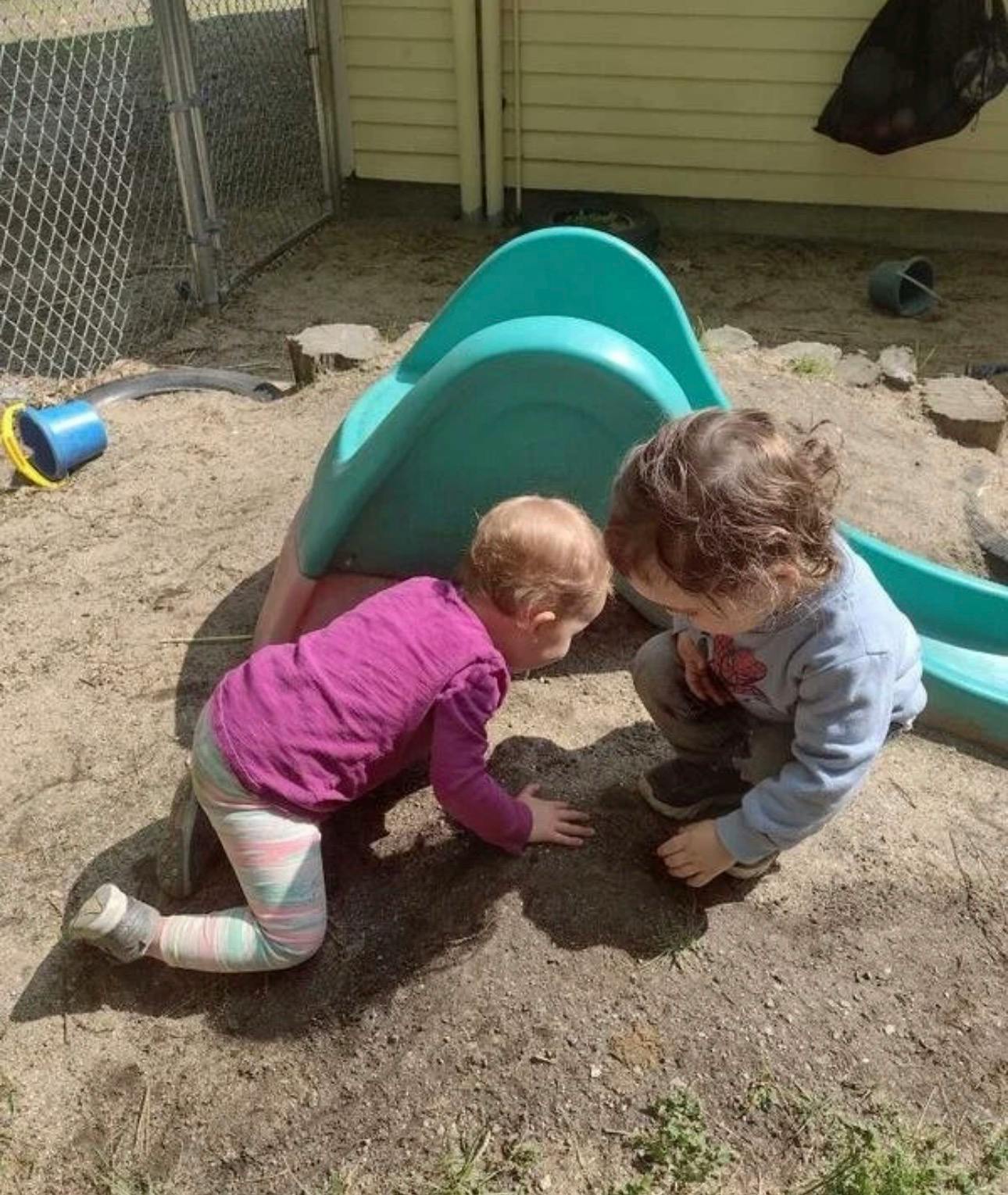 Two children playing in dirt next to a small slide