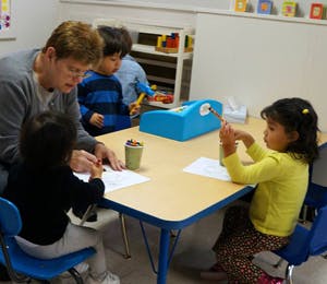 Adult and three children drawing at a table in a classroom