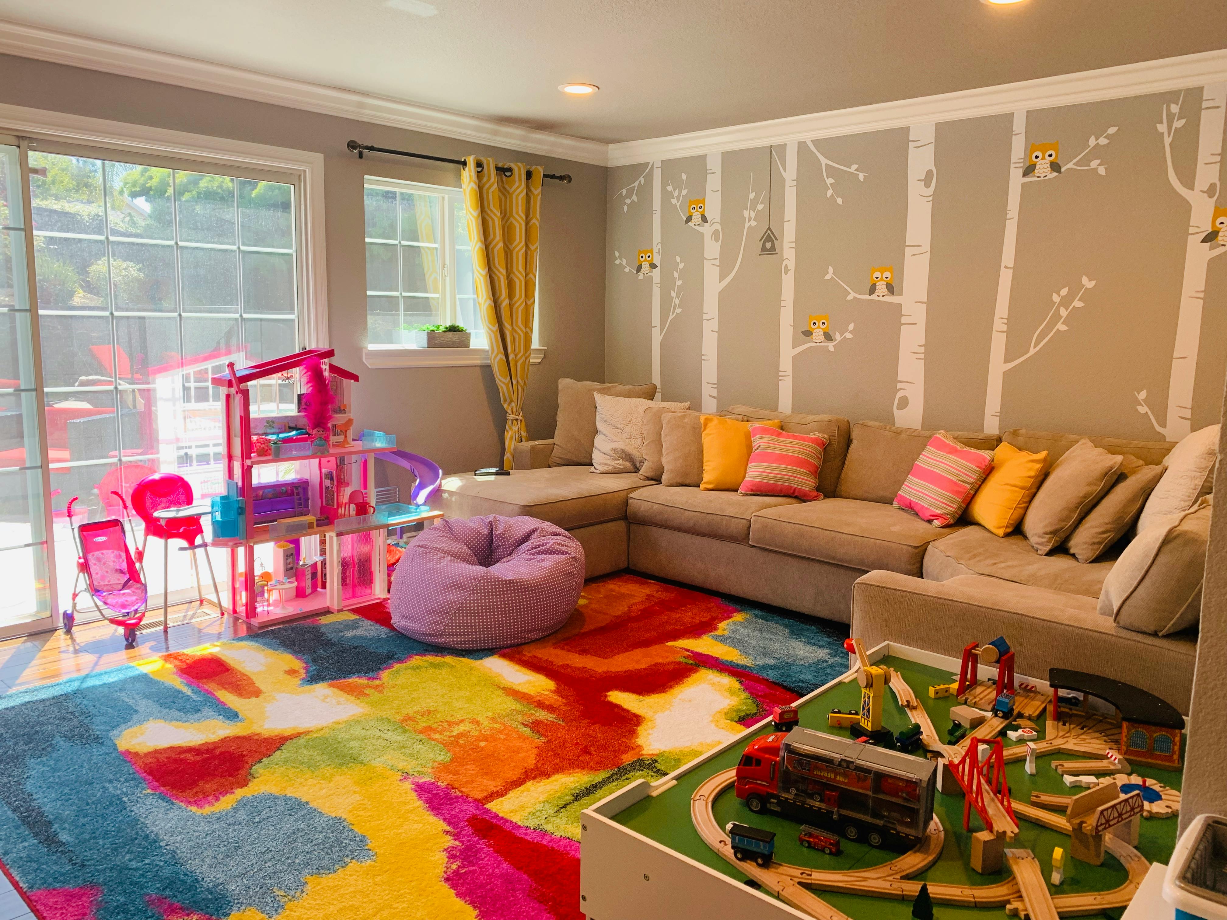 Playroom with a colorful rug, sofa, dollhouse, and train set
