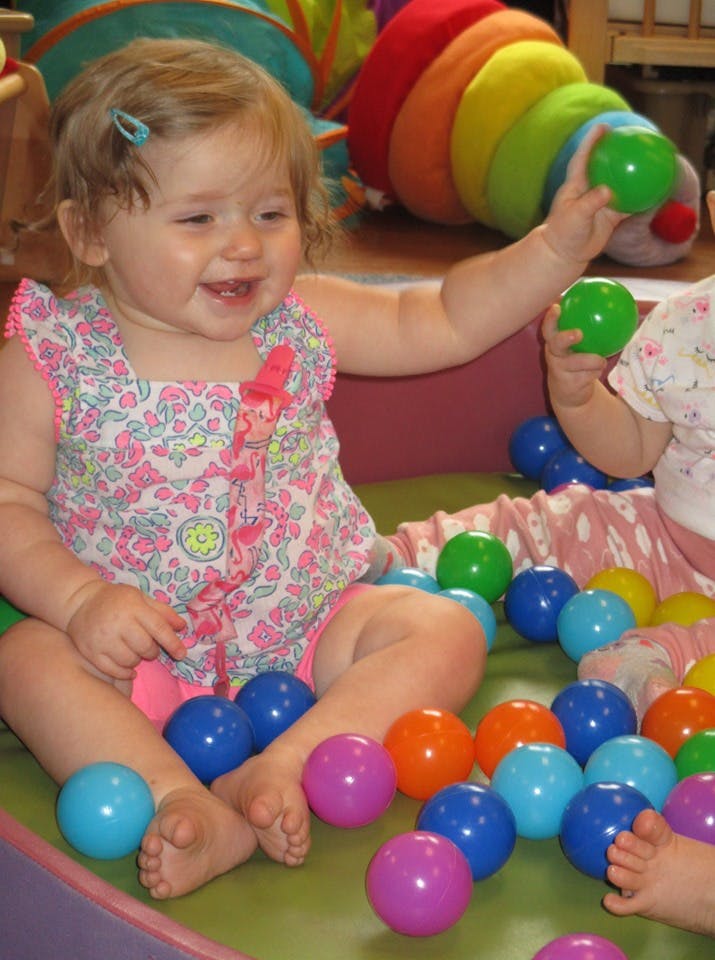 Child sitting in a ball pit, holding a green ball