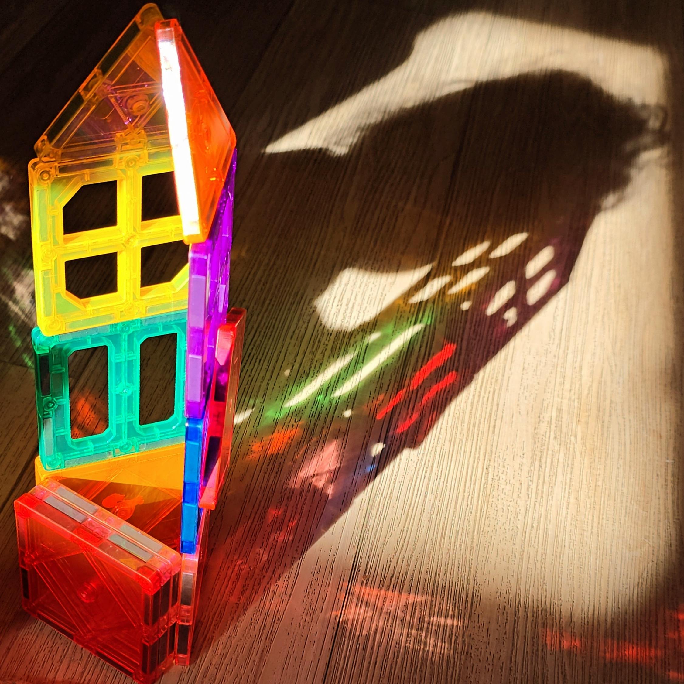 Colorful translucent magnetic tiles casting shadows and light patterns on a wooden surface