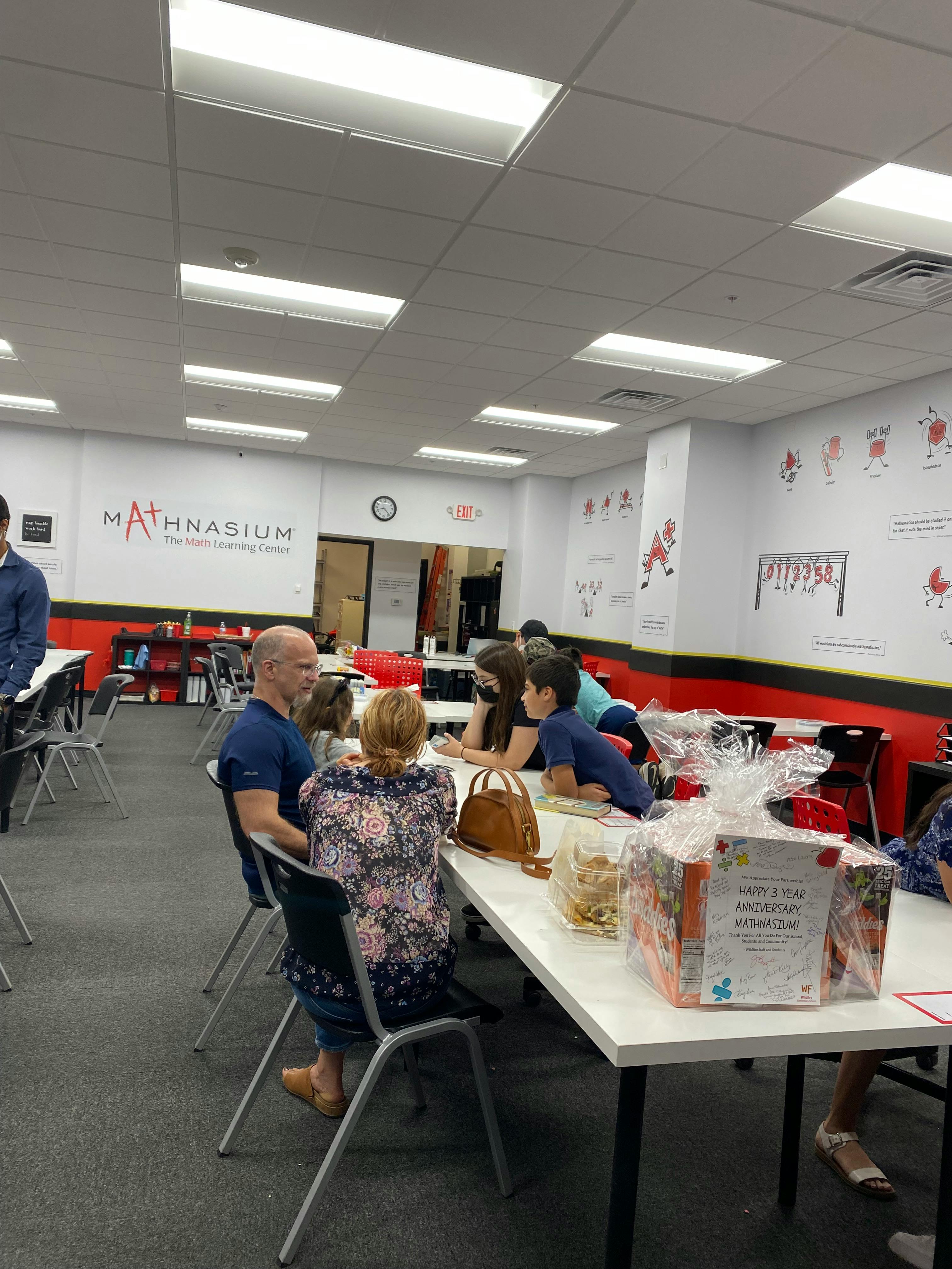 People sitting at tables in a room with a Mathnasium sign