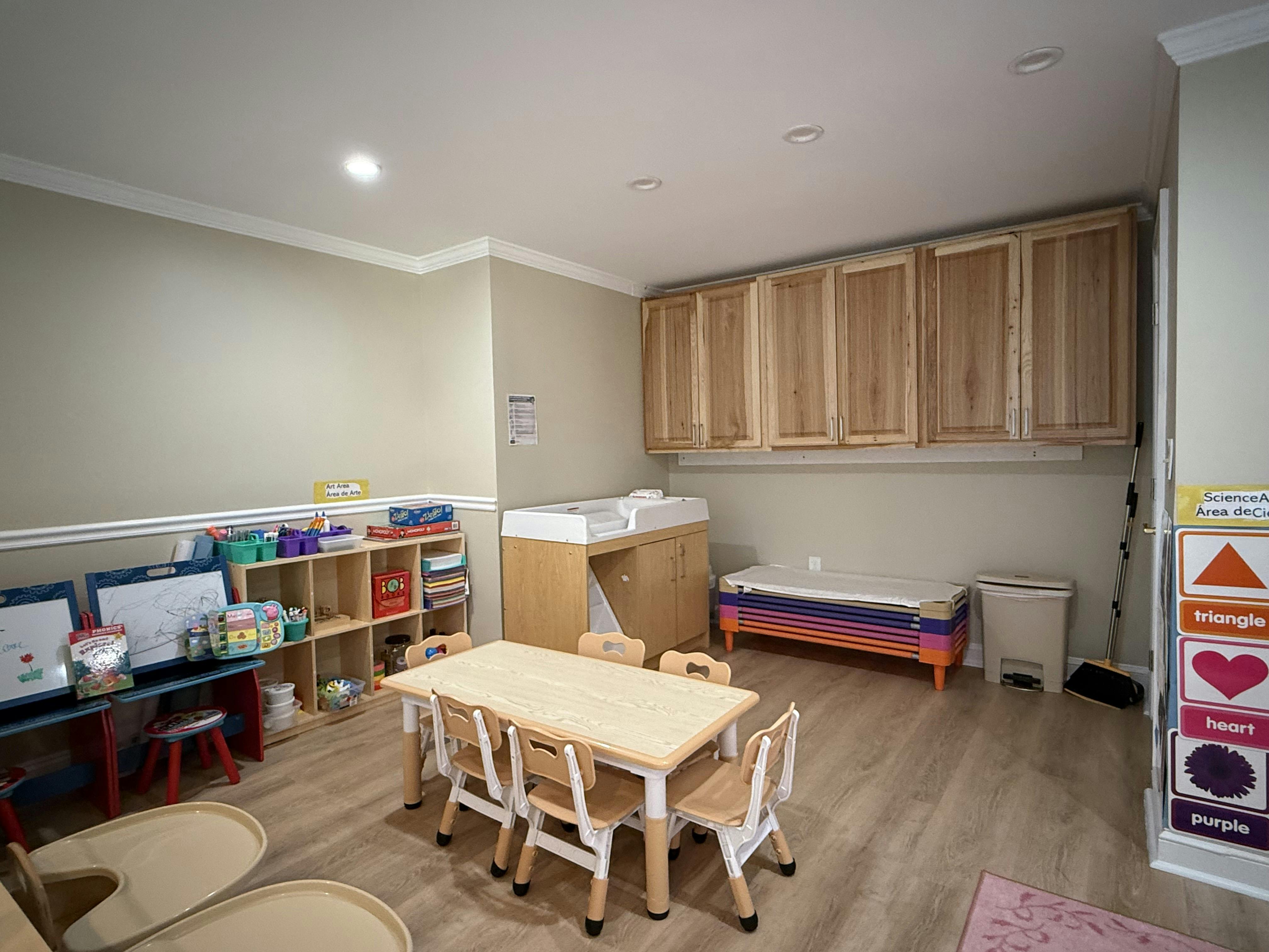 Children's classroom with small tables and chairs, shelving, and a changing station