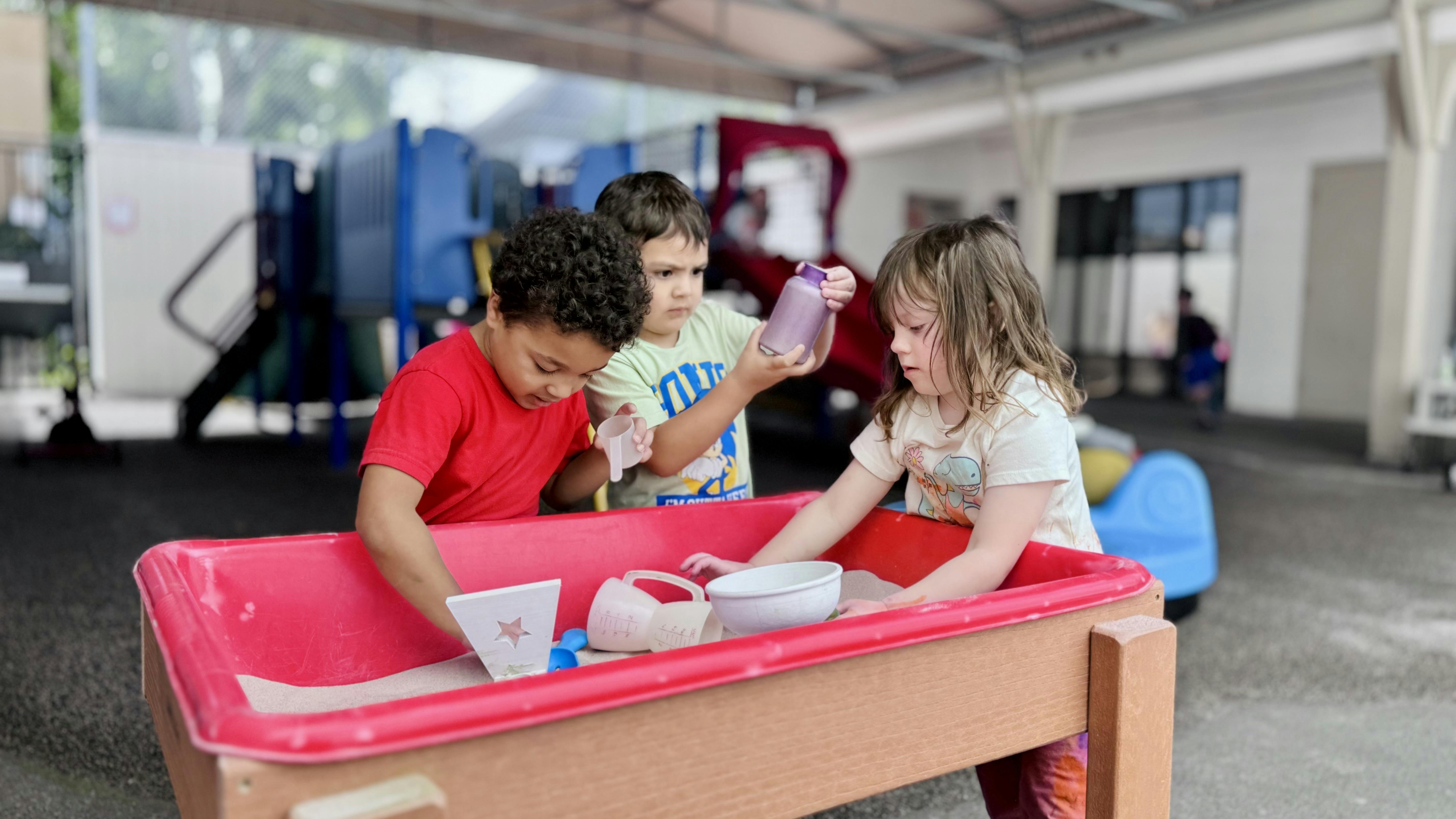 Three children playing in a sand table
