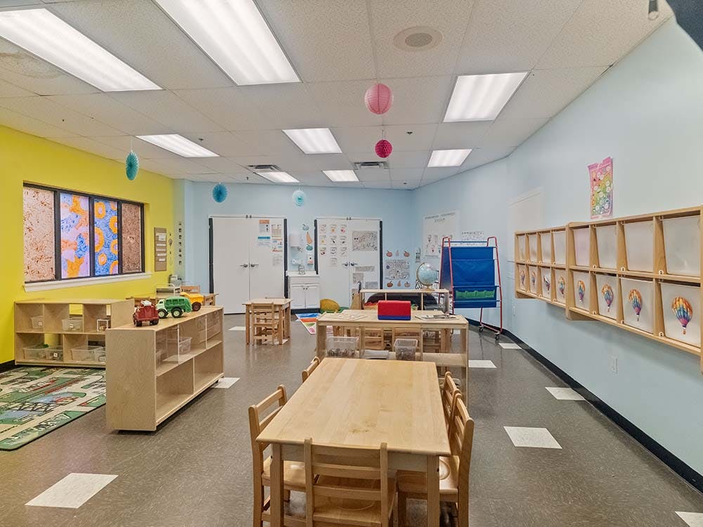 Colorful classroom with small tables and chairs, shelves, and learning materials