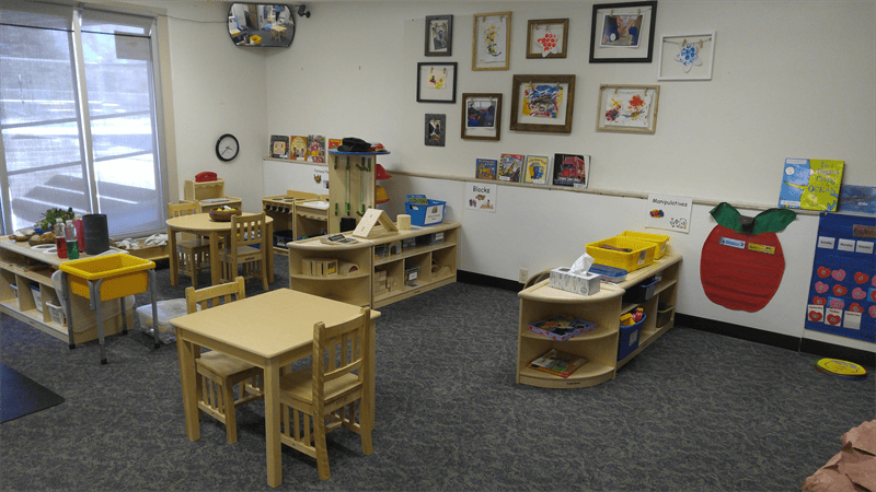 Classroom with small tables and chairs, shelves, and artwork on the walls