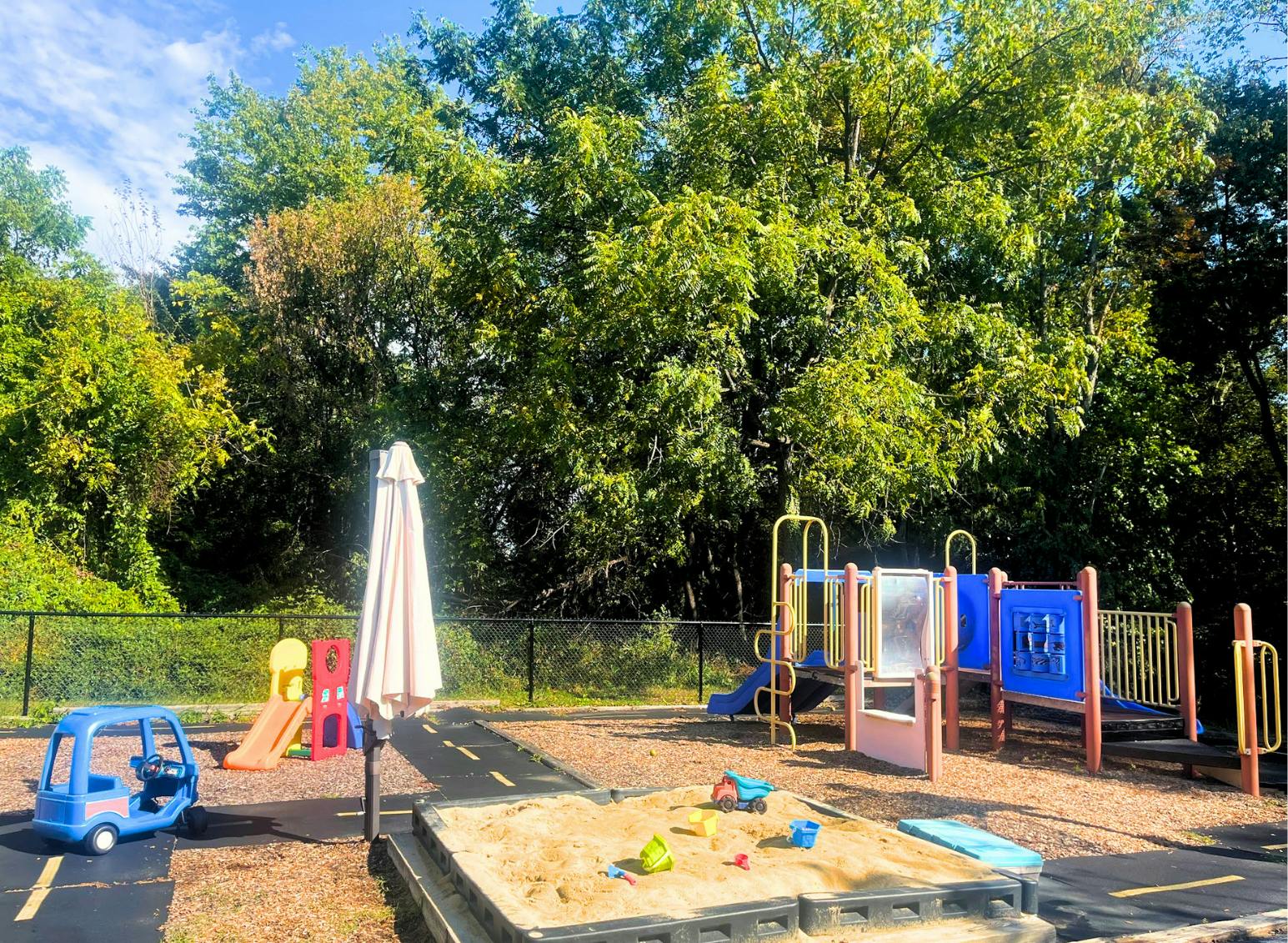 Playground with a sandbox, toy car, and play structures under trees