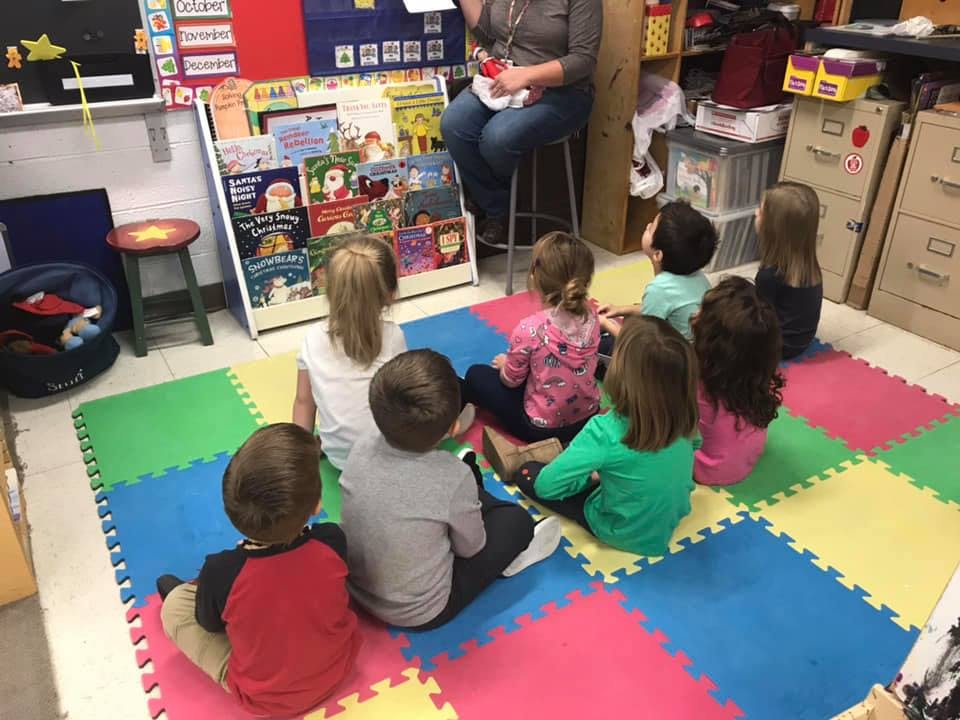 Person reading to children sitting on a colorful mat in a classroom