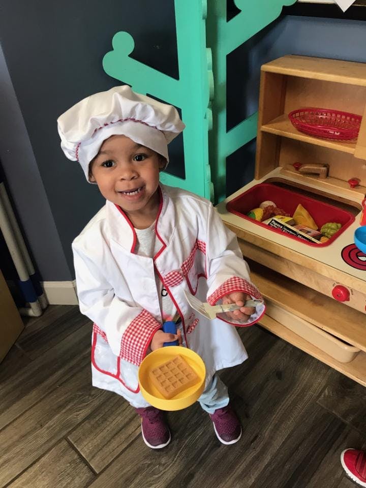 Child in chef's hat and coat holding a toy waffle in a pan