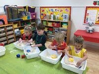 Four children playing with sensory bins in a classroom