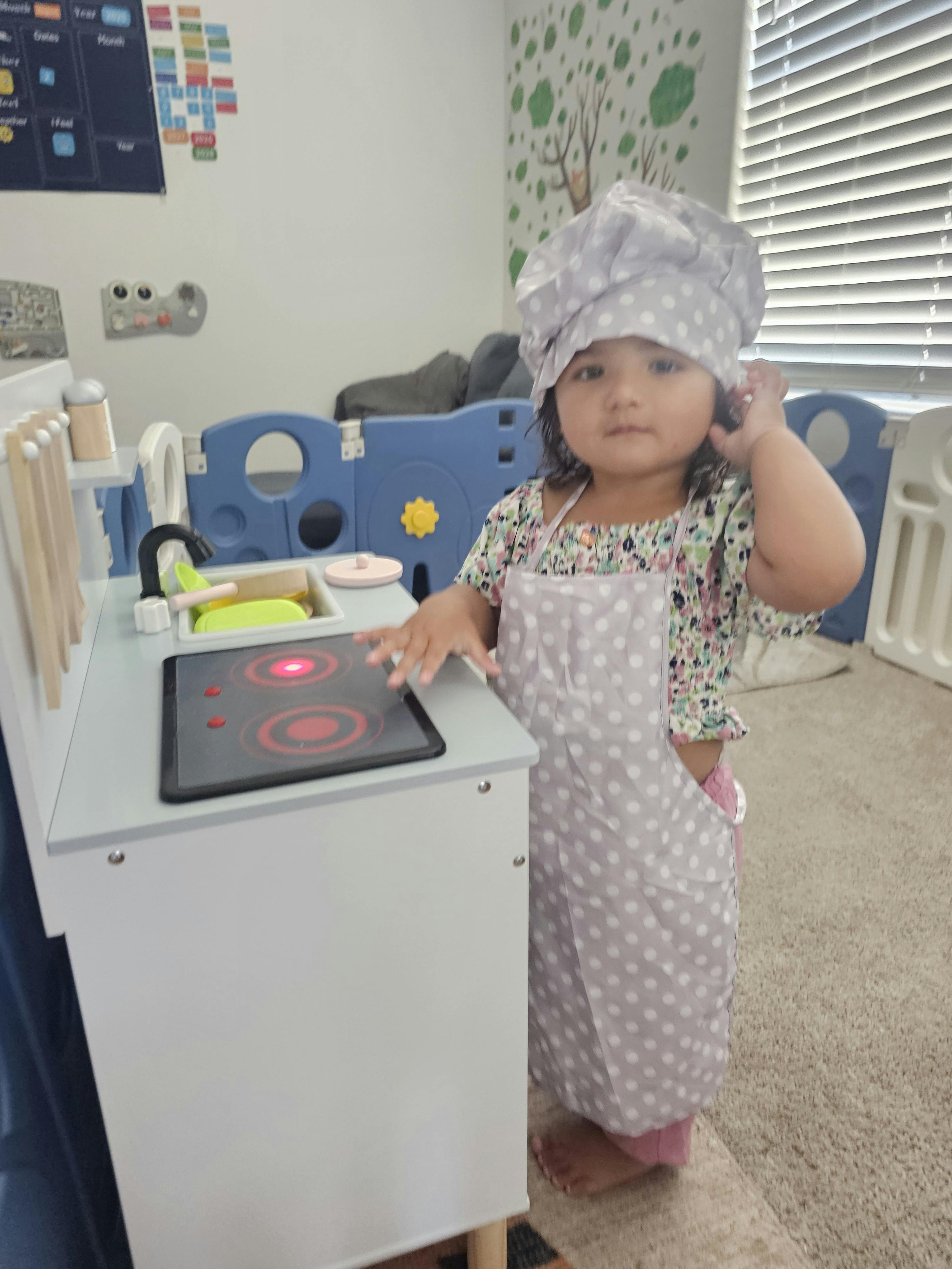 Child in a chef hat and apron playing with a toy kitchen