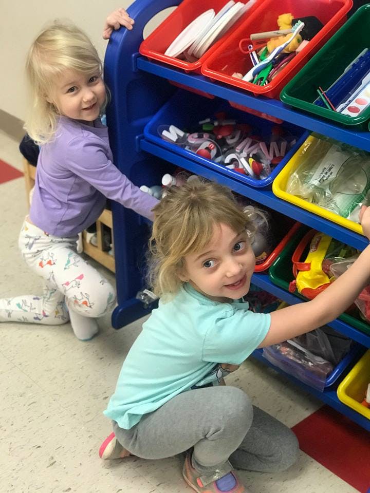 Two children reaching into storage bins in a classroom