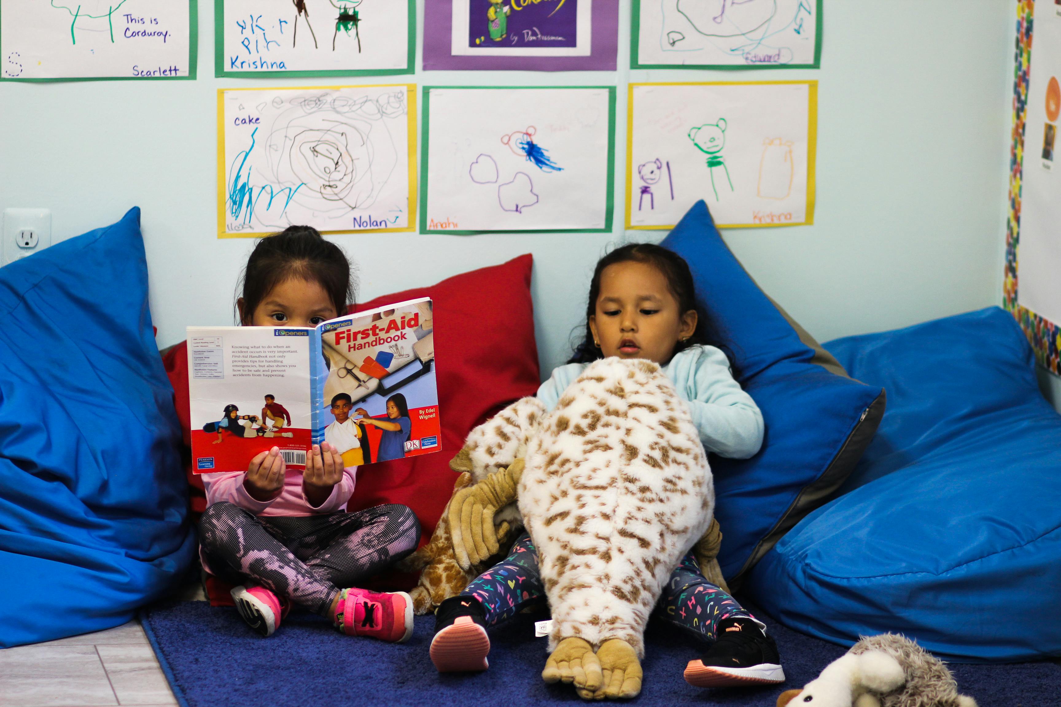 Two children sitting on beanbags, one reading a book, the other holding a stuffed animal
