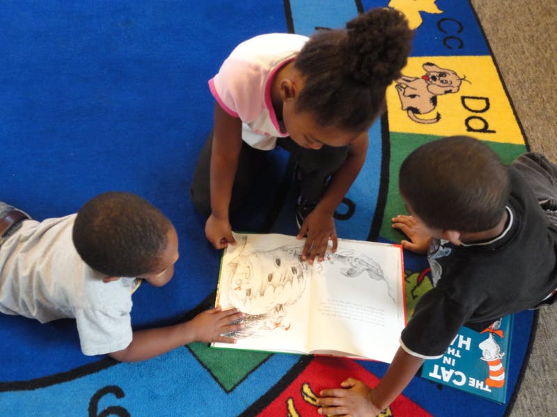 Three children looking at a book on a colorful rug