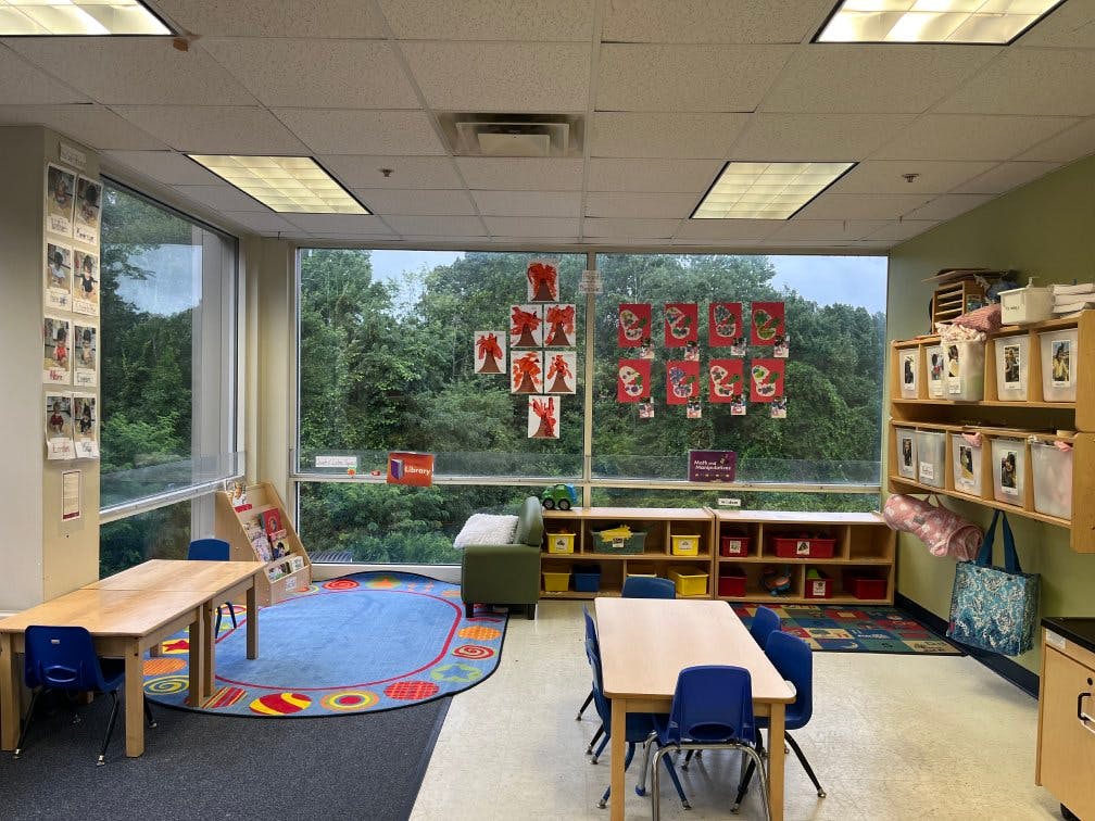 Classroom with tables, chairs, colorful rug, shelves, and window art