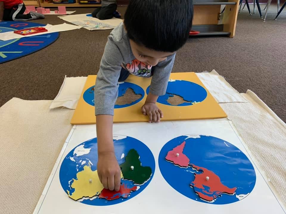 Child playing with a world map puzzle on the floor