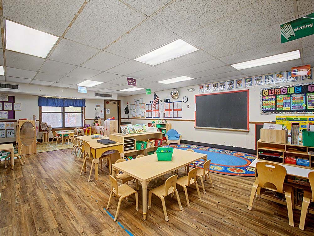 Empty classroom with small tables and chairs, and a chalkboard