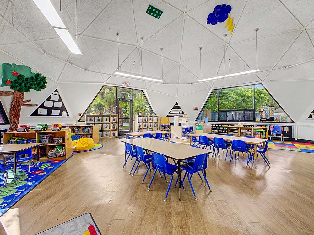 Classroom with tables and blue chairs arranged in groups, a large window view