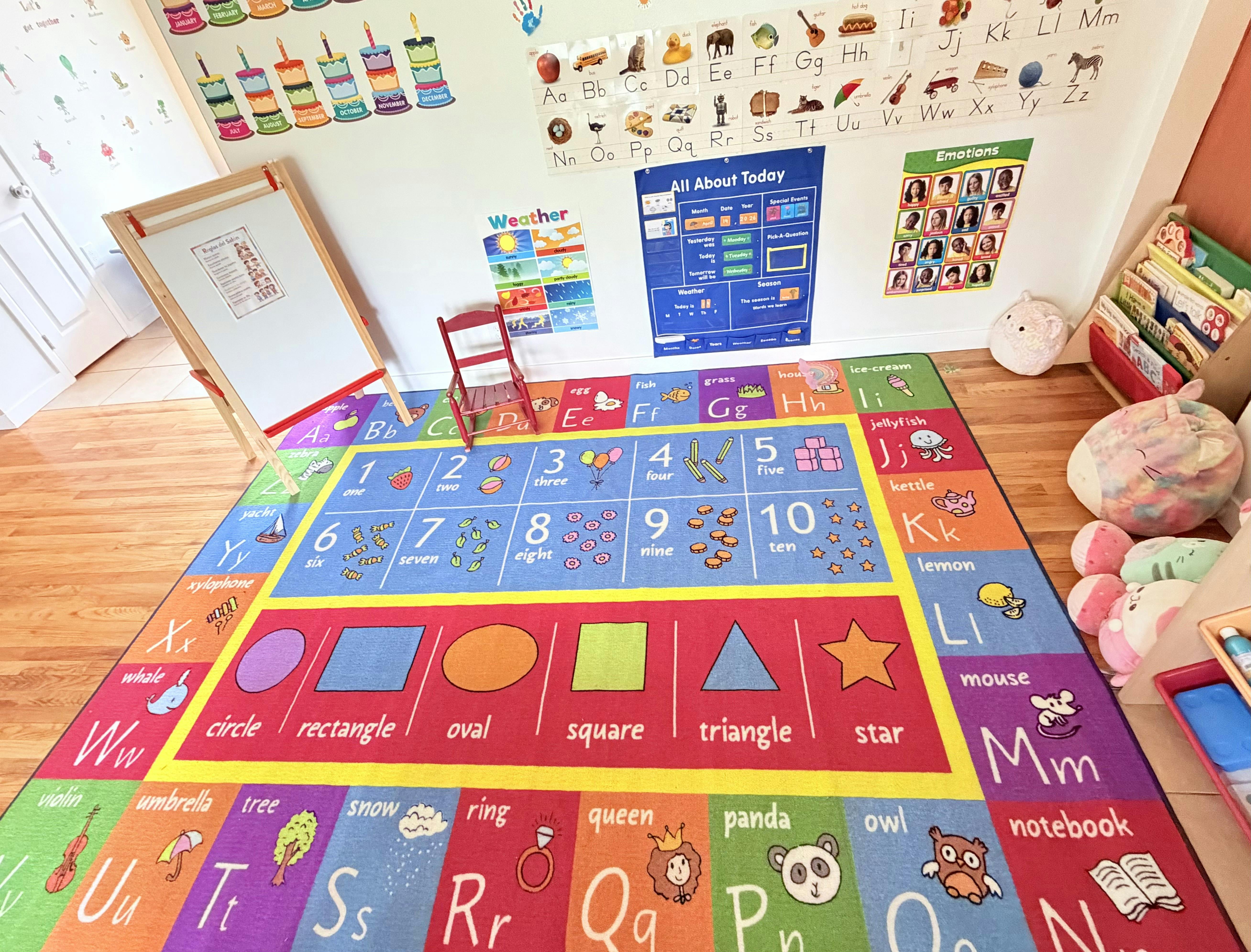 A colorful classroom rug with letters, numbers, and shapes, surrounded by educational wall charts