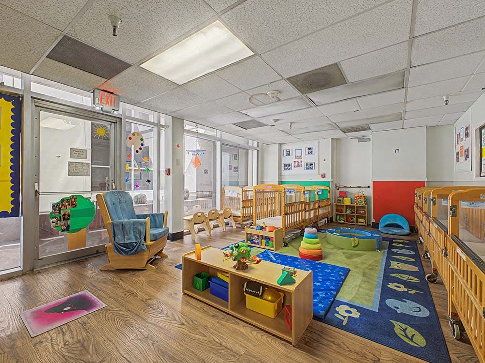 A colorful childcare classroom with cribs, playmats, and a rocking chair