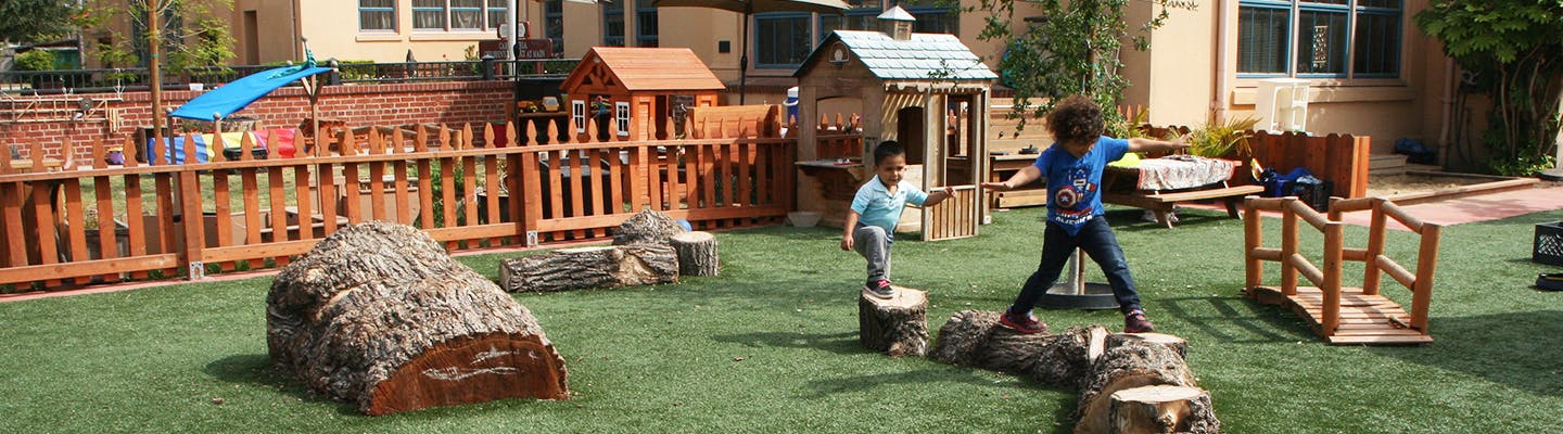 Two children balancing on logs in a playground