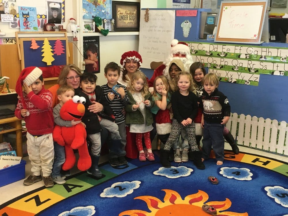 Adults and children in a classroom, some dressed in Santa hats