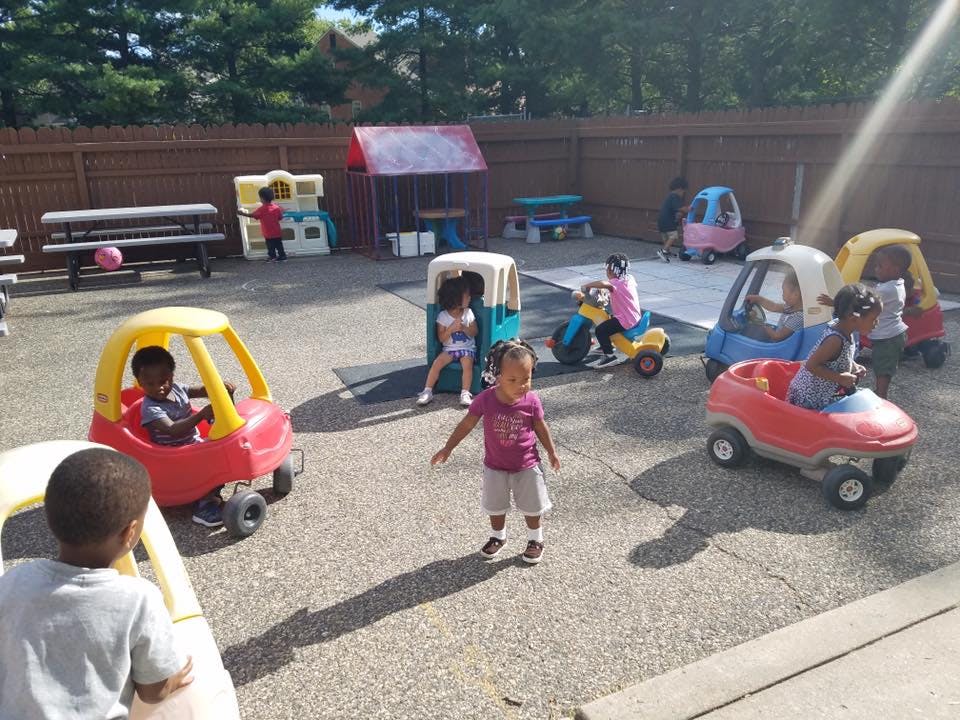 Children playing with ride-on toys in a fenced outdoor area