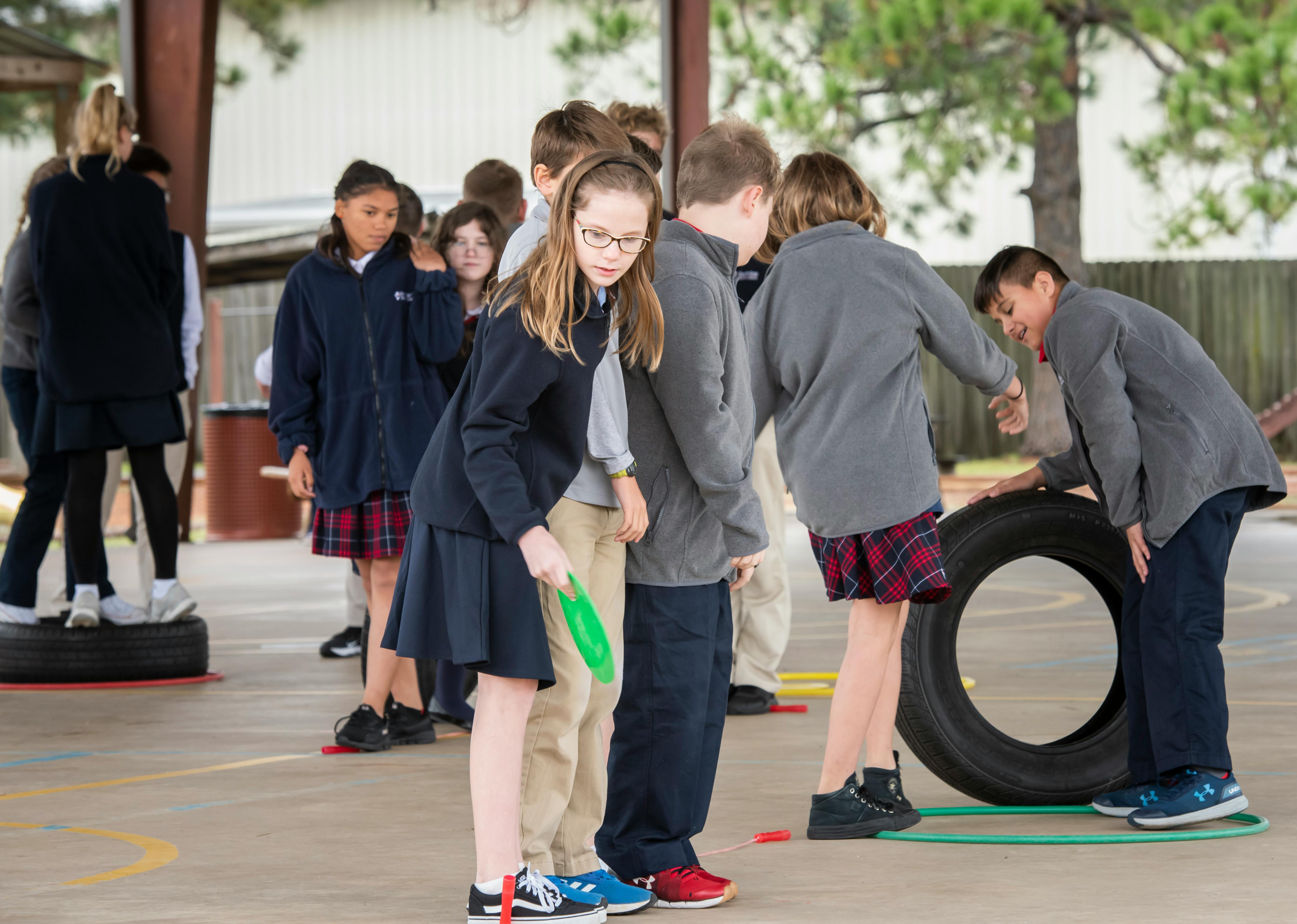 Children in school uniforms playing with tires and hoops on an outdoor court