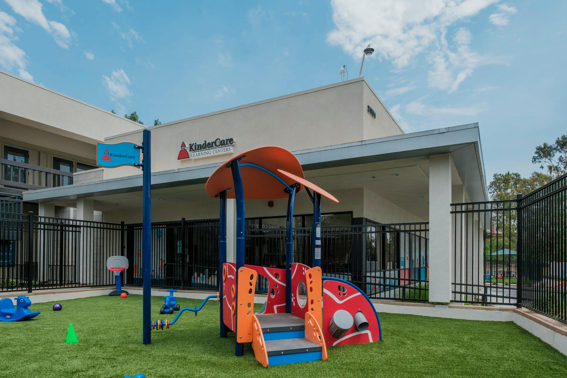 Playground area with red and blue play structure, basketball hoop, and green turf