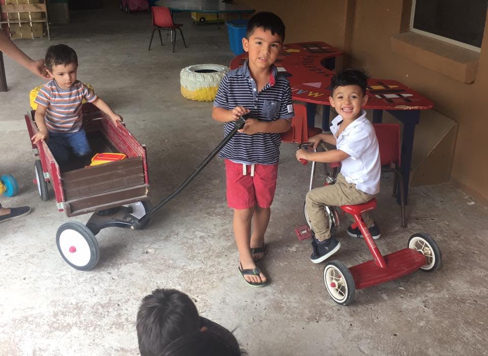 Three children playing with a wagon and a tricycle