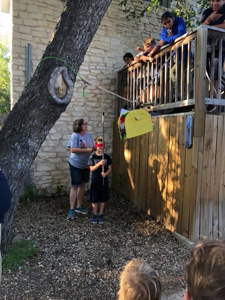 Child blindfolded with a stick about to hit a taco-shaped piñata
