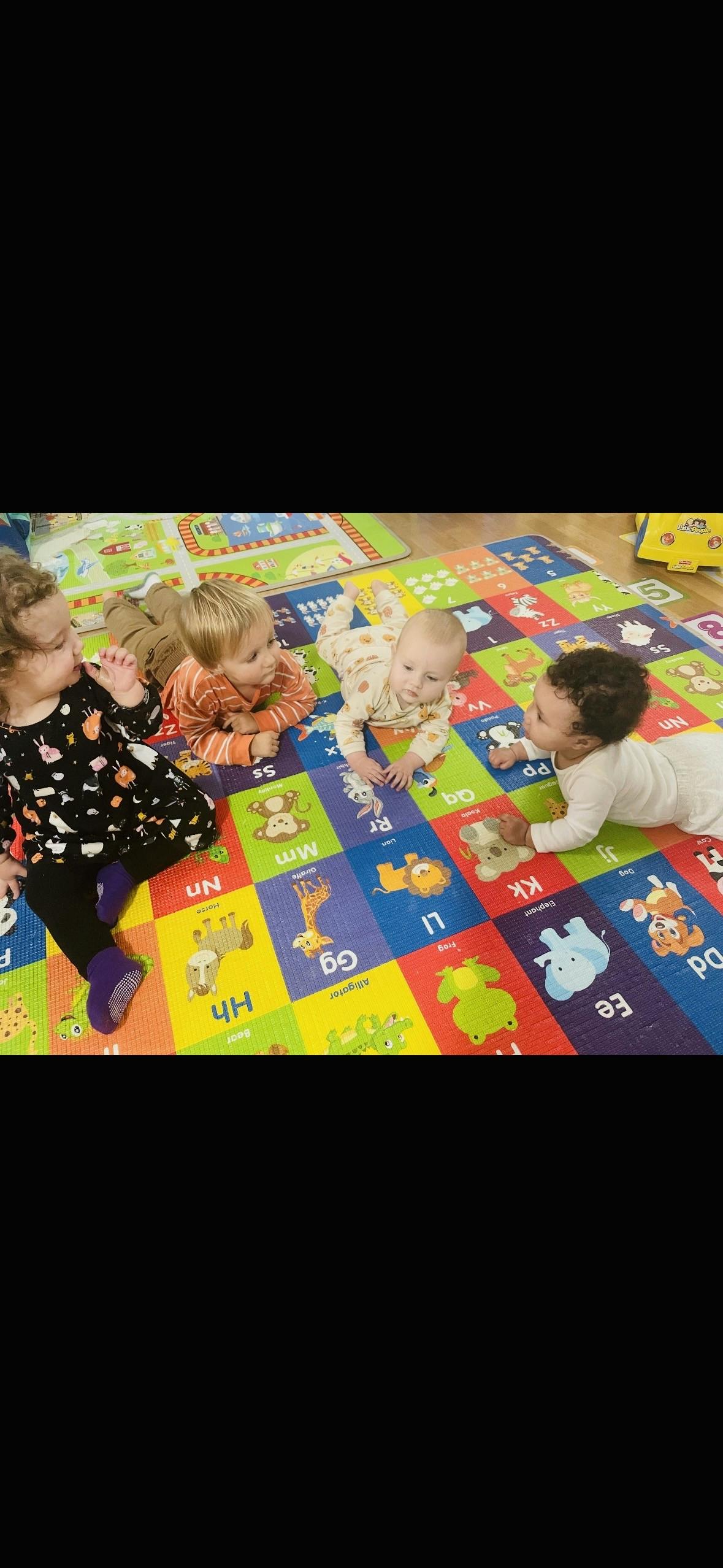Four young children playing on an alphabet mat