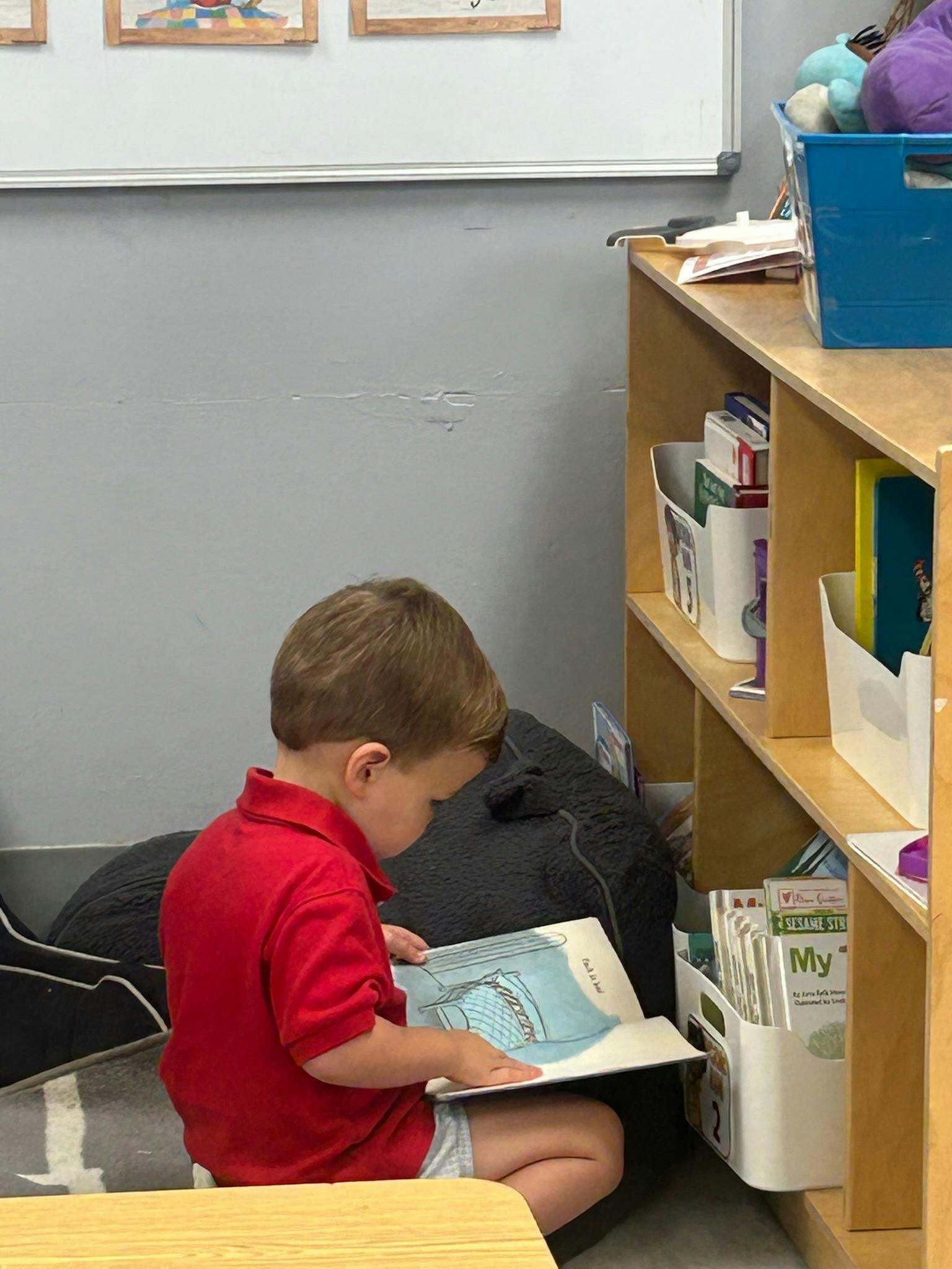Child sitting on a floor cushion reading a book in a classroom