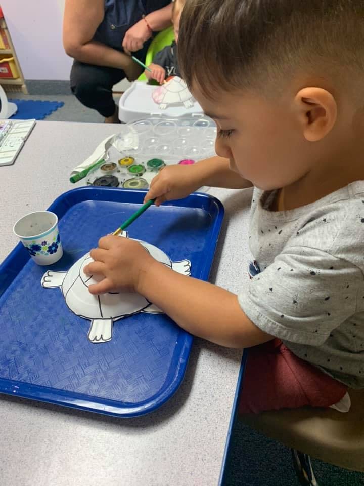 Child painting a paper turtle on a blue tray