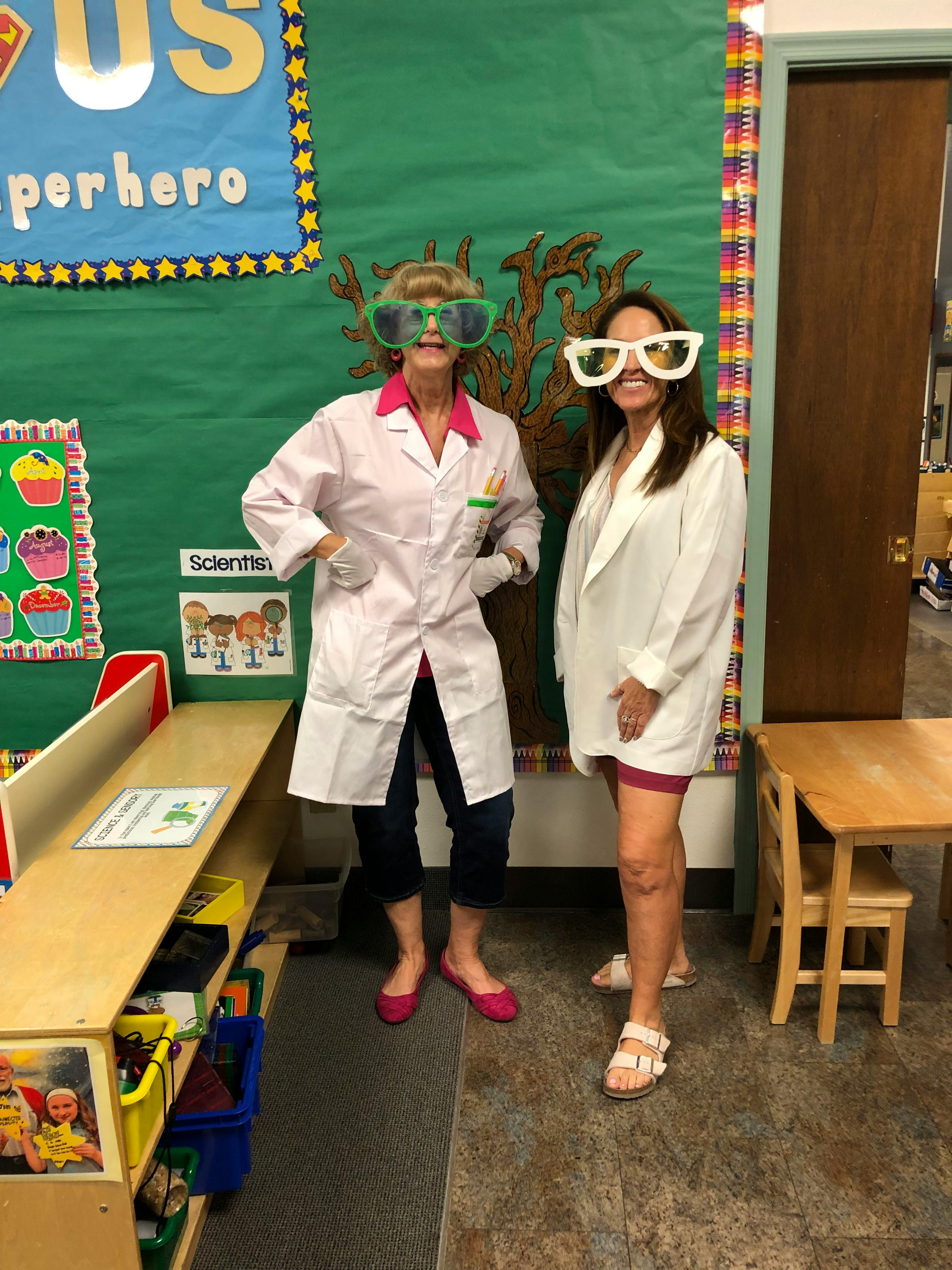 Two people in lab coats and novelty glasses standing in a classroom