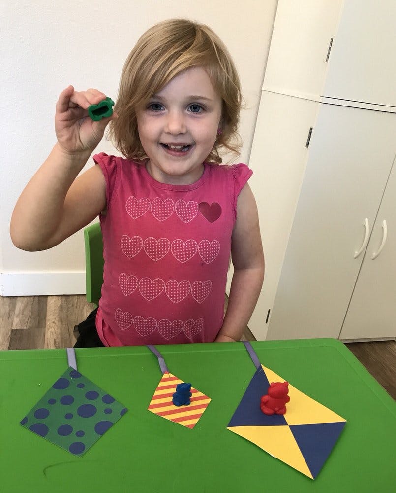 Child holding up a small green object, with paper crafts on a table