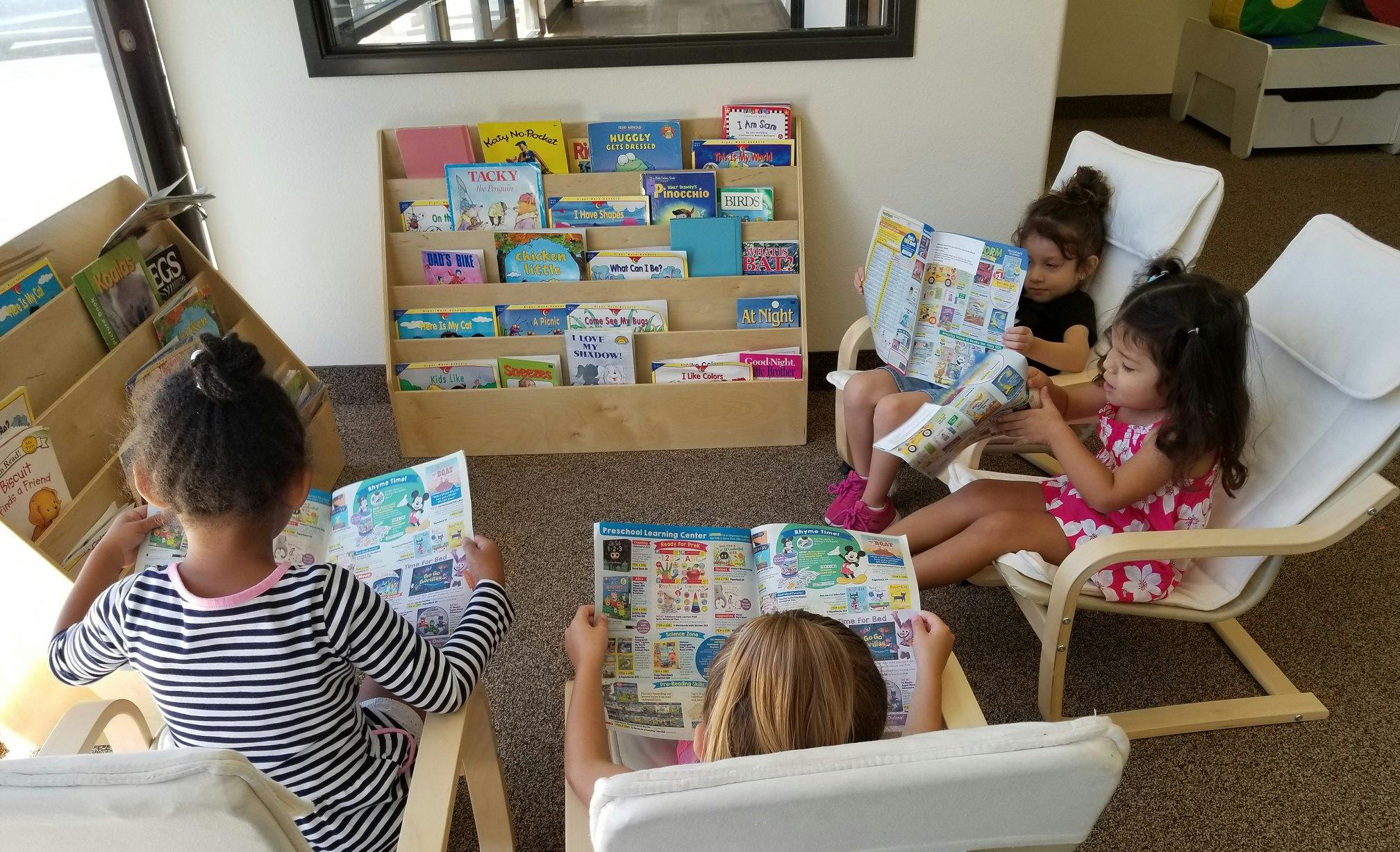 Four children sitting in chairs reading books