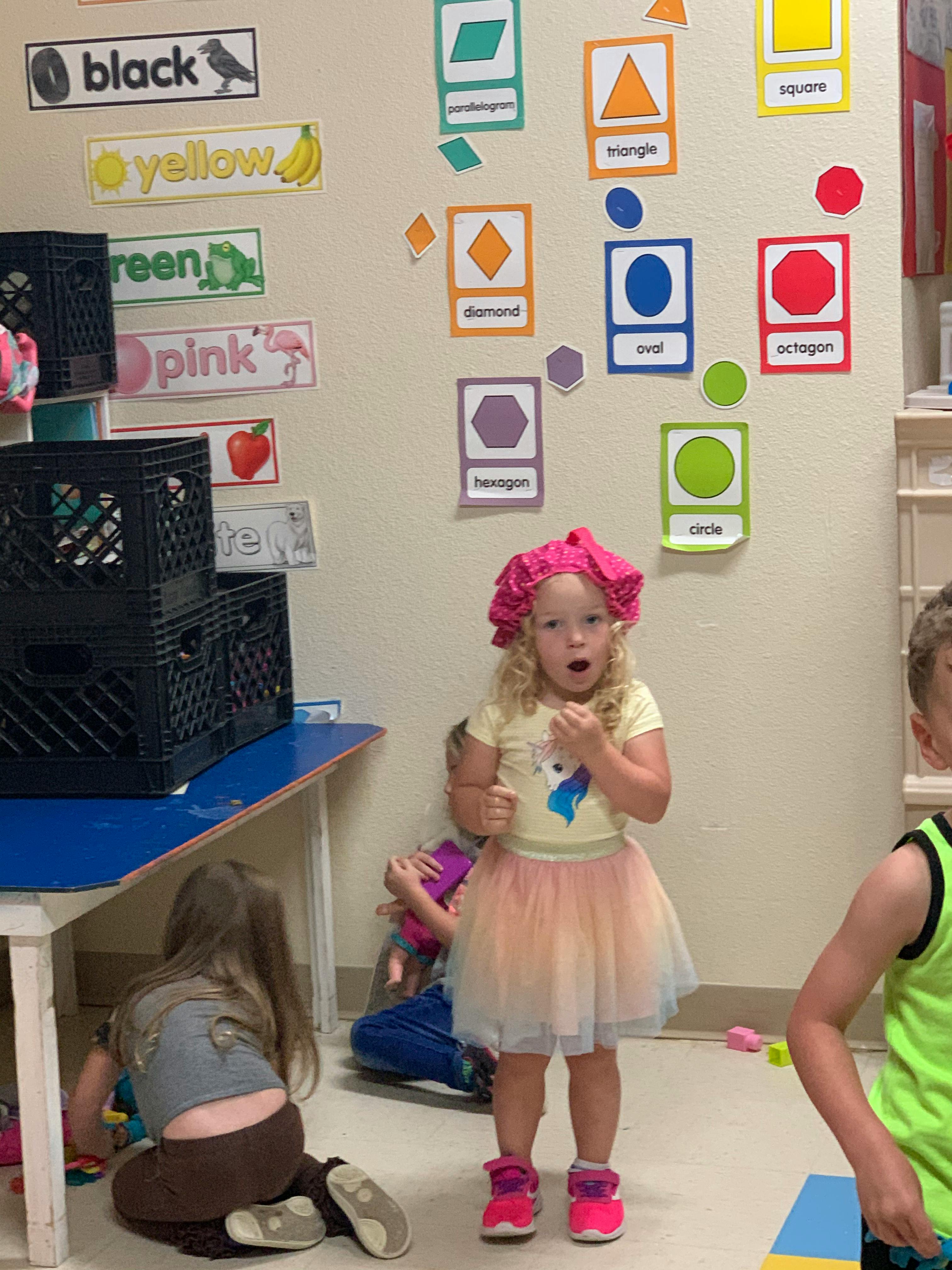 Child in a pink ruffled hat and tutu standing in a classroom